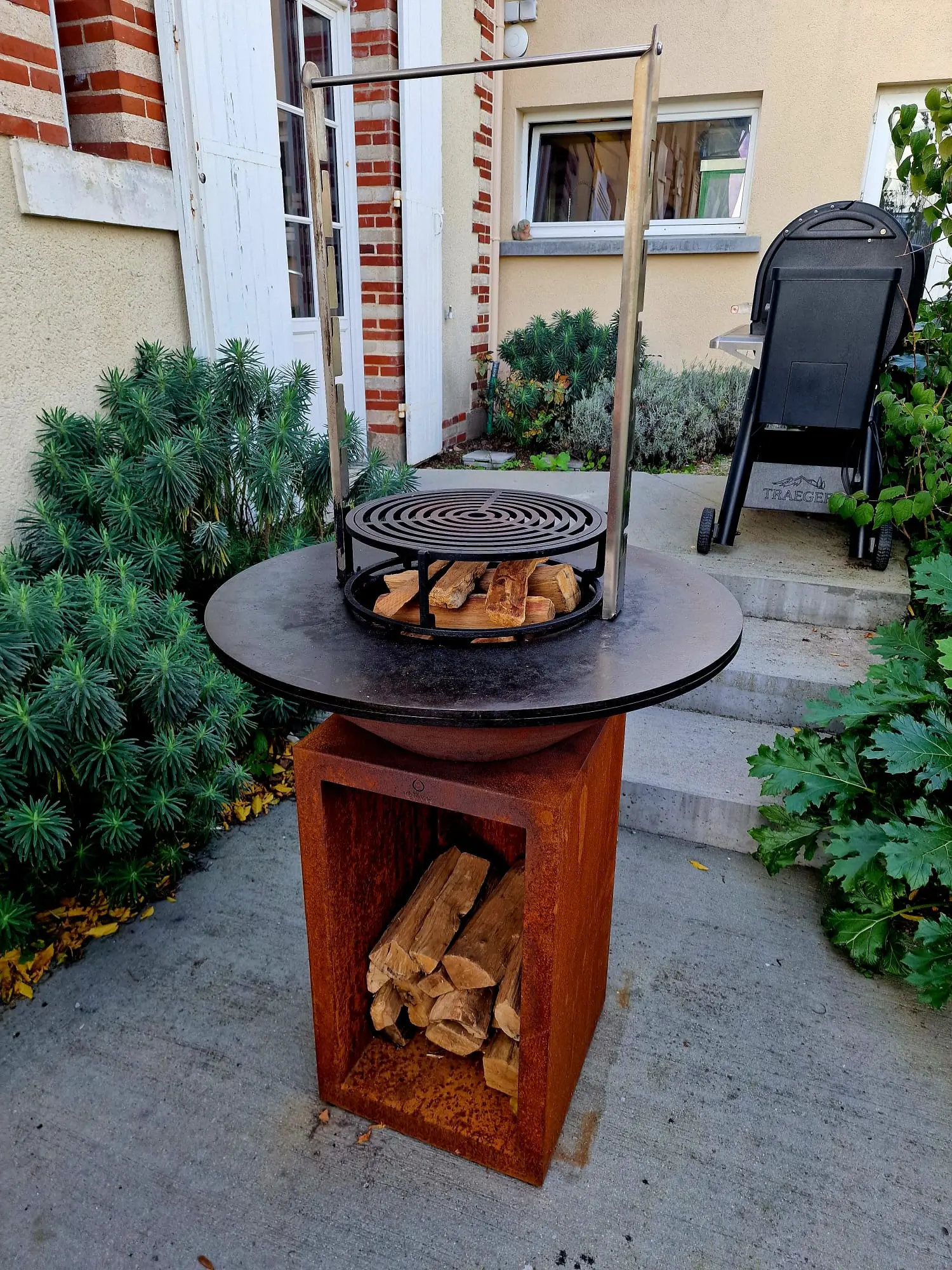 Brasero OFYR avec sa grille et ses bûches, installé dans une cour